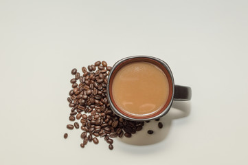 Coffee in a mug sitting beside a pile of beans against a white background