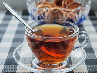 On the table there is a transparent glass Cup with tea on a glass saucer and a glass vase with bagels.