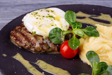 A piece of steak with egg paschot, served with puree potatoes and cherry tomatoes with greens