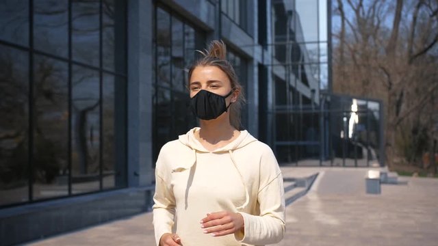 Portrait of beautiful young and fit woman running and jogging alone in business city center area wearing protective face mask