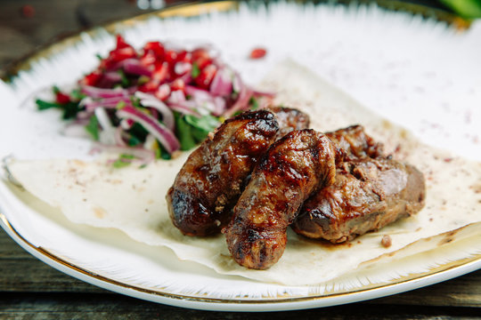  Restaurant dish on a wooden background with vegetables. Azerbaijani pork kidneys with onions on pita bread.