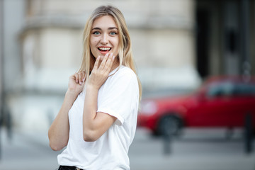 Beautiful blonde girl stand at city street with long hair flying on the wind, hold her black small...