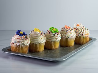 5 yellow cupcakes with white swirled frosting and colorful fondant flowers and sprinkles on top...