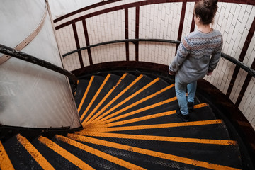 Young woman dressed in jeans and a gray sweater goes down some black and yellow spiral stairs to access the subway.