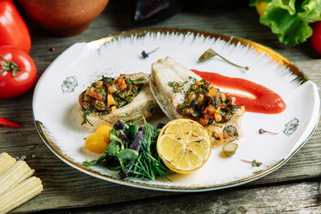Restaurant dish with vegetable decor on a wooden background. Sea fish fried on a plate with sauce.