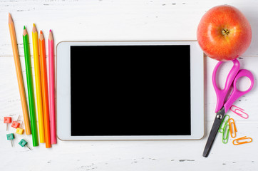 A tablet with an empty screen and office supplies on a white wooden background. Concept app for...