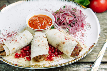 Restaurant dish on a wooden background with vegetables. Lula kebab in lavash with pomegranate and onion on a plate.