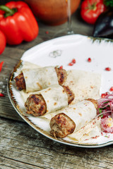 Restaurant dish on a wooden background with vegetables. Lula kebab in lavash with pomegranate and onion on a plate.