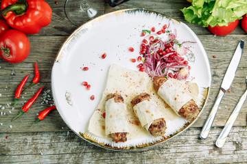 Restaurant dish on a wooden background with vegetables. Lula kebab in lavash with pomegranate and onion on a plate.