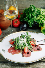  Restaurant dish on a wooden background with vegetables. Salad with beef tenderloin and arugula on a plate.