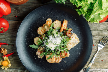  Restaurant dish on a wooden background with vegetables. Salad with shrimp, avocado and arugula on a plate.