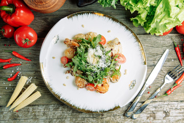  Restaurant dish on a wooden background with vegetables. Salad with shrimp, avocado and arugula on a plate.