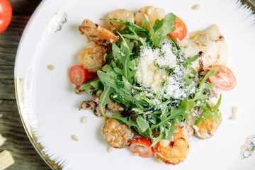  Restaurant dish on a wooden background with vegetables. Salad with shrimp, avocado and arugula on a plate.
