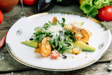  Restaurant dish on a wooden background with vegetables. Salad with shrimp, avocado and arugula on a plate.