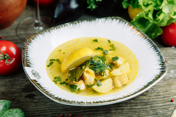Restaurant dish on a wooden background with vegetables. Soup with fish and seafood and lemon on a plate.