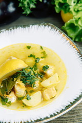 Restaurant dish on a wooden background with vegetables. Soup with fish and seafood and lemon on a plate.