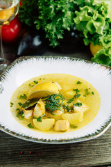 Restaurant dish on a wooden background with vegetables. Soup with fish and seafood and lemon on a plate.