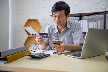 Senior Asian man using smart phone shopping online and paying with credit card at home