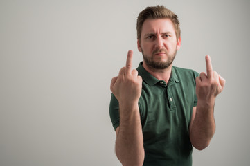 Portrait of serious stylish attractive man with thick beard, dressed in casual green t shirt showing double obscene gesture