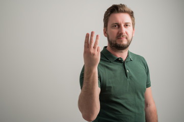 Portrait of serious stylish attractive man with thick beard, dressed in casual green t shirt showing number three