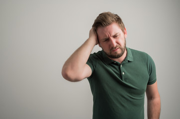 Fototapeta na wymiar Portrait of serious stylish attractive man with thick beard, dressed in casual green t shirt gesturing head ache