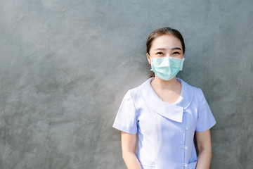 Asian nurses wear protective masks and look at the camera. The background is a cement wall.