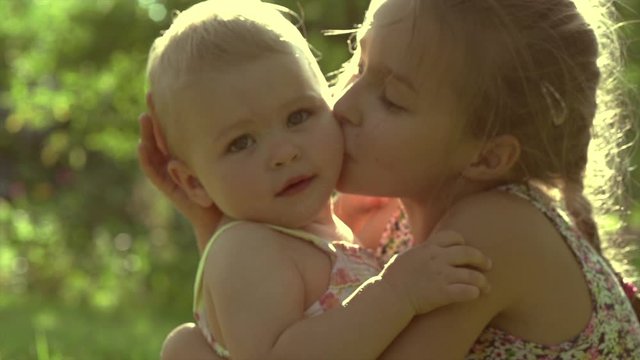 Happy Little Girls Playing together outdoor, laughing, hugging and kissing. Playful siblings, sisters outside. Family Love concept. Slow motion 4K UHD video