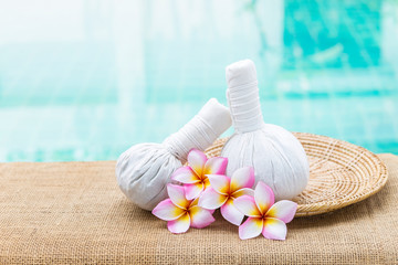 Thai herbal massage ball with plumeria flower on rattan tray over blurred blue water background, outdoor day light, spa object