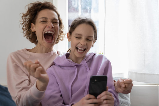 Excited overjoyed family young adult mom and teenage girl daughter feeling euphoric winning using smartphone at home. Happy parent and child getting great ecommerce sale offer, celebrating success.