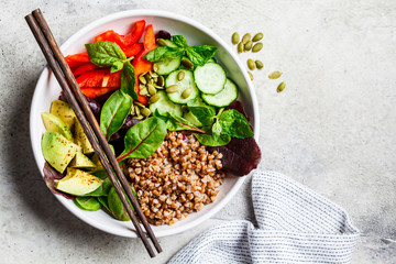 Buddha bowl salad with buckwheat, vegetables and seeds in white plate, top view.