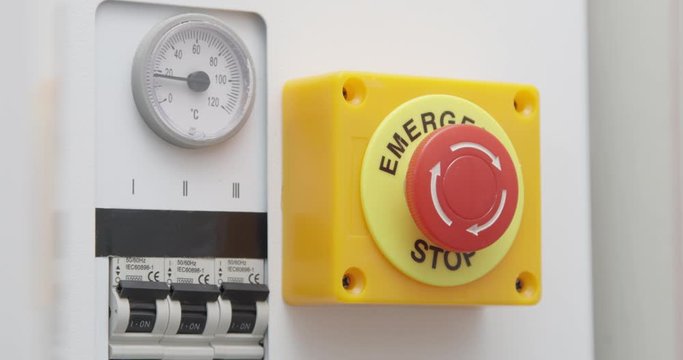 Hand Pressing Emergency Stop Red Button on the Control System Panel with Electricity Switch
