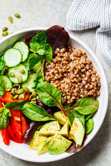 Buddha bowl salad with buckwheat, vegetables and seeds in white plate, top view.