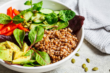Buddha bowl salad with buckwheat, vegetables and seeds in white plate.