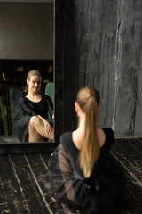 Fototapeta na wymiar Reflection attractive ballerina practicing ballet in pointe shoes, sitting in front of a black mirror.