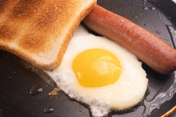 scrambled eggs, toast and sausage fried in a pan.