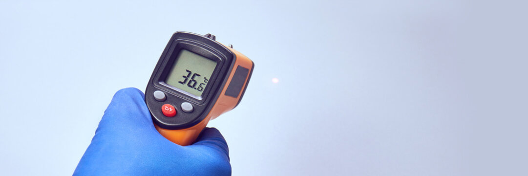 hand in blue glove holds ir thermometer high temperature