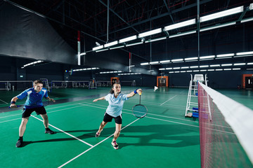 Mixed double playing badminton game, woman jumping and swinging racket to beat off shuttlecock - obrazy, fototapety, plakaty