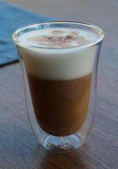 Hot cappuccino in clear glass on wooden table.