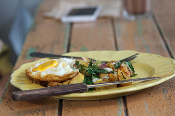 One fried egg and potatoes with fork and knife on yellow plate.