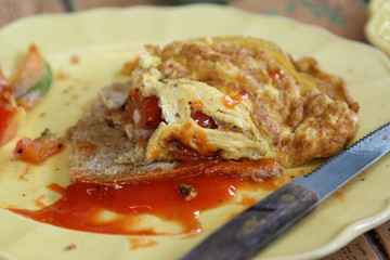 Breakfast; omelet, bread and ketchup on the side on yellow plate.