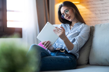Concentrated young woman using her digital tablet while sitting on sofa at home.