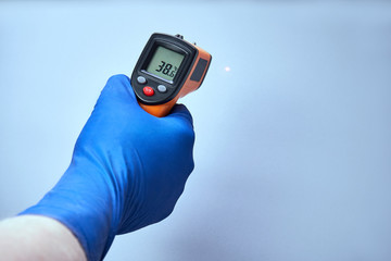 hand in blue glove holds ir thermometer high temperature