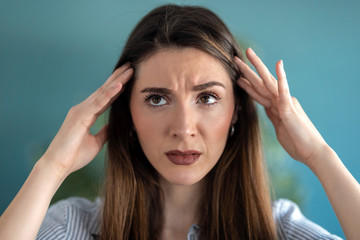 Frustrated young woman with headache and frowning while looking to side at home.