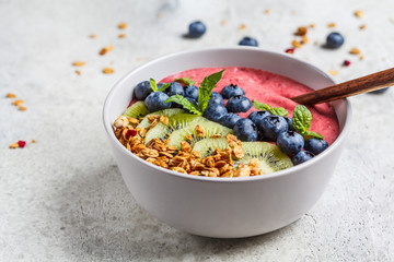 Pink berry smoothie bowl with granola, kiwi and blueberries, light background.