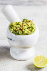 Cooking guacamole - avocado sauce in a white stone mortar.