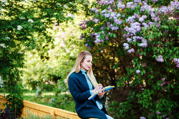 Smiling caucasian woman, young student is making notes, studying outdoors in the countryside in spring. 