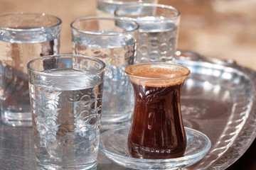 Glasses of water and Turkish coffee are on a metal tray