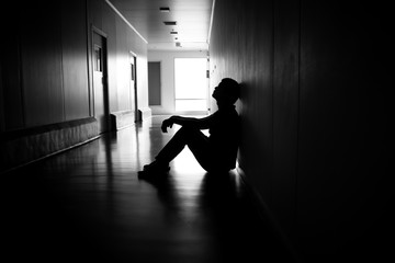 Silhouette of depressed man sitting on walkway of residence building. Sad man, Cry, drama, lonely...