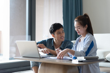 A young asian couple is sitting on a carpet using a computer