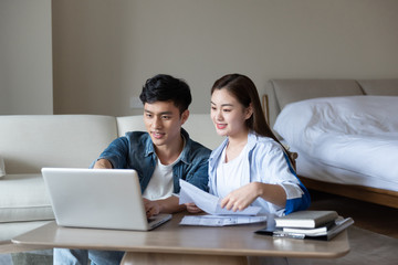 Obraz premium A young asian couple is sitting on a carpet using a computer